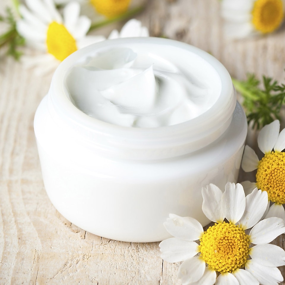 A tub of white face cream on a table surrounded by flowers