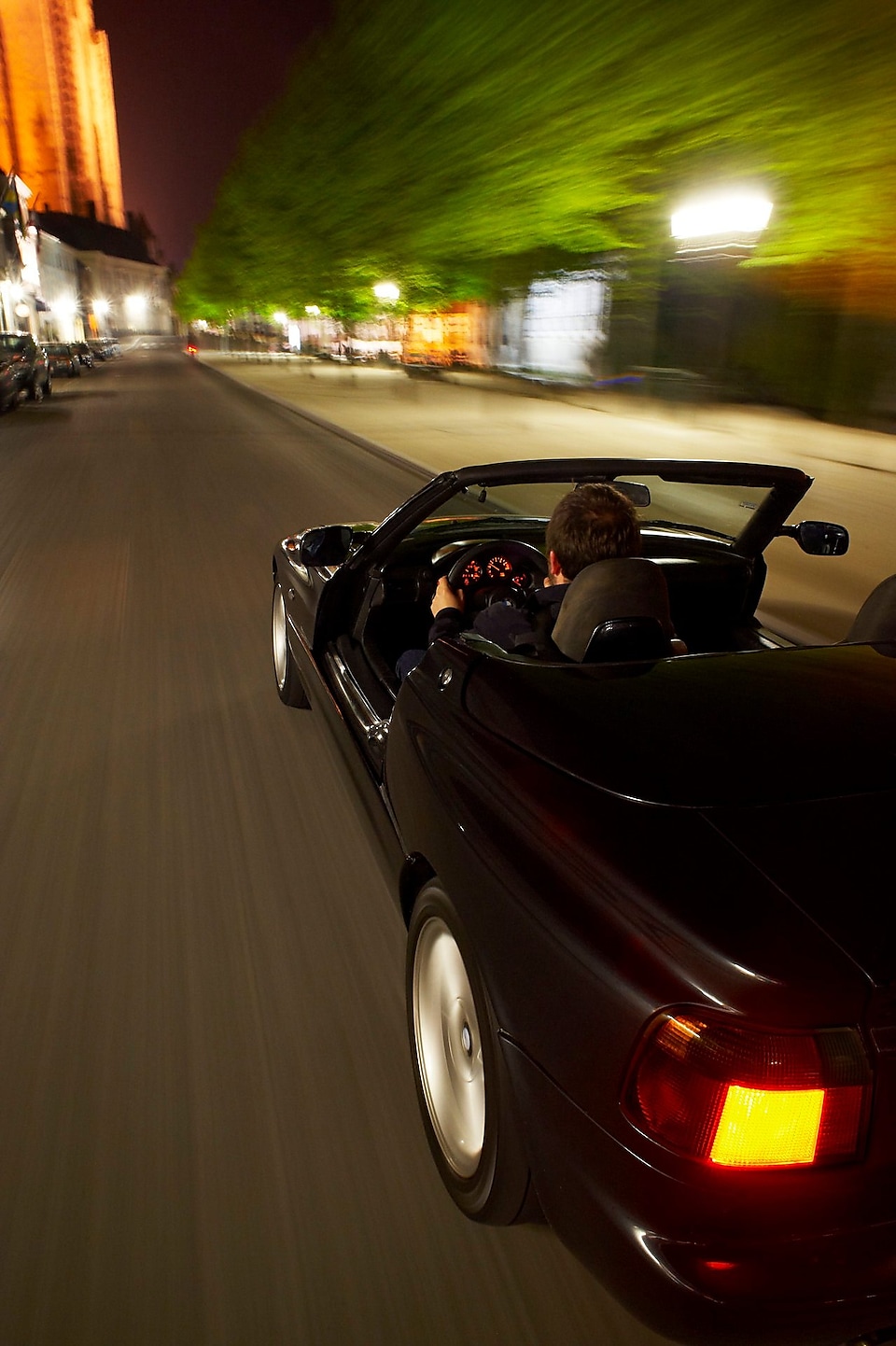 Black convertible car driving through Brugge streets at night