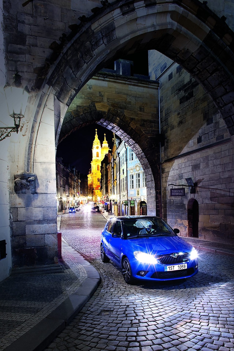 Blue car parked under an arch on a cobbled Prague road at night