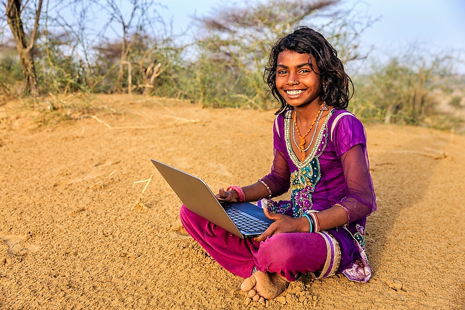 Young girl from India sitting on sand using a laptop
