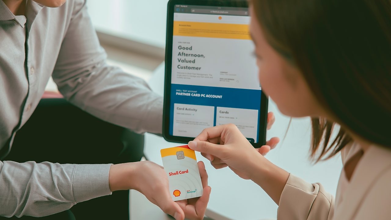 a woman and a man are sitting on a desk looking at tablet and card