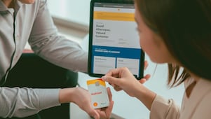 a woman and a man are sitting on a desk looking at tablet and card