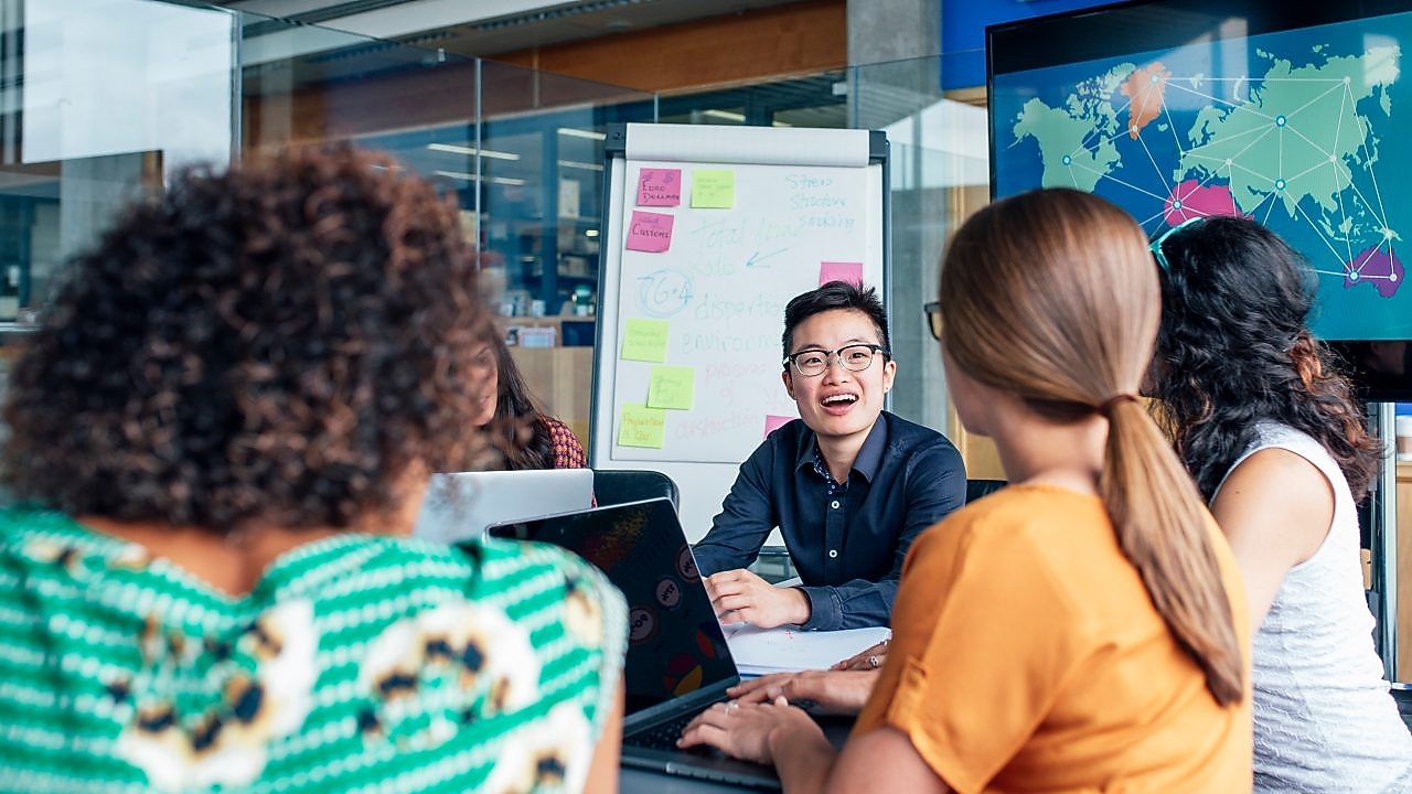 นักธุรกิจสี่คนนั่งรอบโต๊ะกลมอ่านเอกสาร พรมสีเทา และสีเหลือง